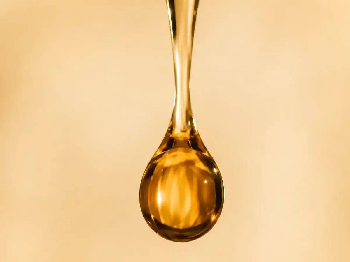 Amber oil droplet macro on warm off-white background